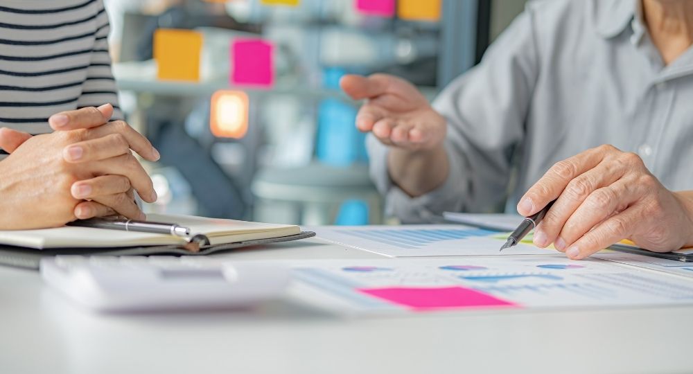 Две женщины обсуждают рабочие документы и записи в блокноте, делятся идеями и планами